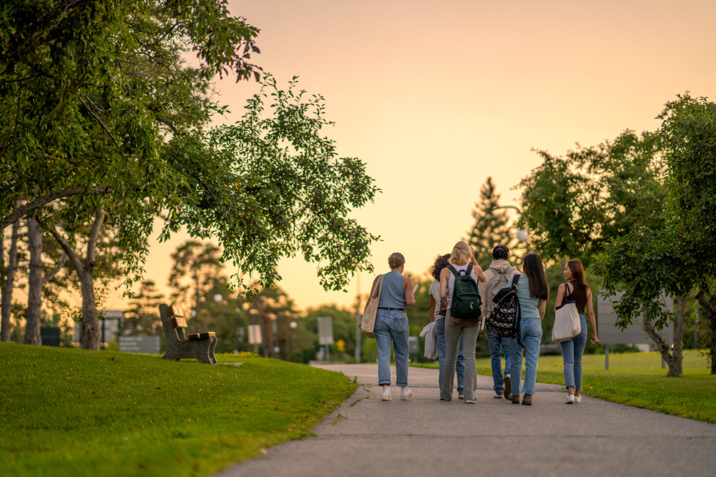 students-on-campus › Antioch University A group of students walking down a path in a college campus at sunset, enjoying the serene beauty of the evening.