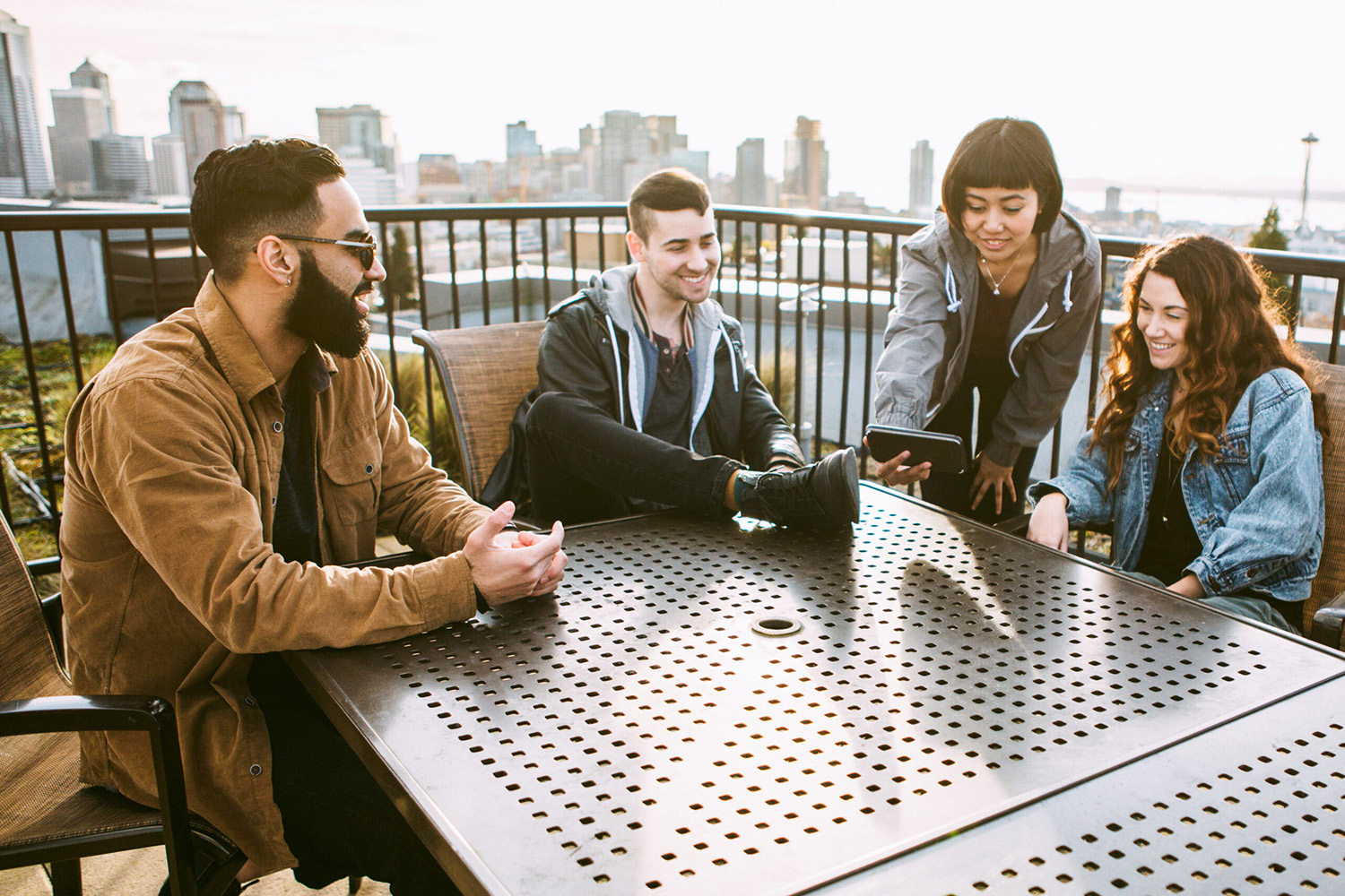 GettyImages-520768618-scaled › Antioch University 4 college aged young adults looking at a phone one is holding out as they sit at a table